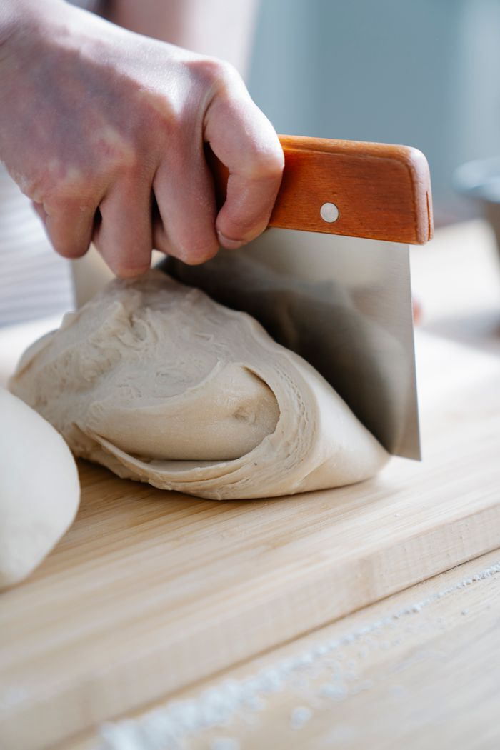 our-journey-03 A hand slicing fresh bread dough with a metal cutter on a wooden board.